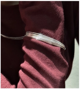 Detail of S925 sterling silver multi-layer wire bracelet worn over a dark knit sleeve