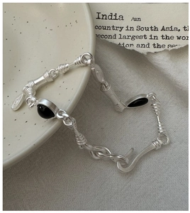 Macro detail of silver bamboo chain bracelet with black onyx stones on a vintage paper