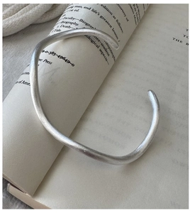 Detail of minimalist S925 silver wave texture cuff on an open book background