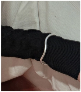 Close-up of a silver wavy textured bangle worn over a black sweater sleeve