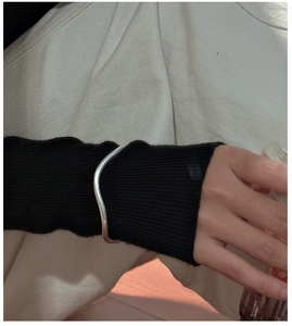 Detail of S925 sterling silver cuff bracelet with wavy texture worn on a black knit sleeve