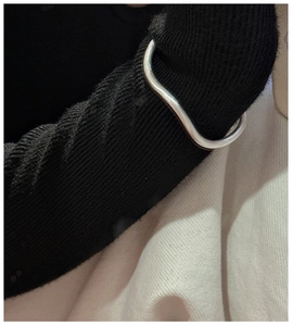 Detailed view of silver wavy textured bracelet styled on black knit sleeve