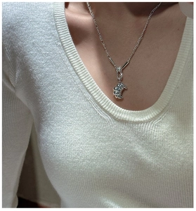 Close-up of a silver croissant pendant necklace on a white knitted sweater