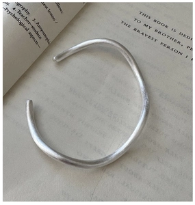 Macro detail of wave-textured S925 sterling silver bangle with matte brushed finish on book