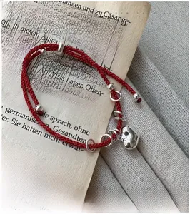 Detailed view of red woven heart bracelet with S925 silver charms on vintage book pages