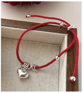 Detail of red braided string bracelet with silver heart charm in a wooden jewelry box