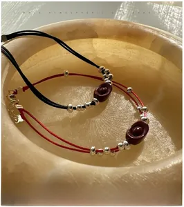 Close-up of S925 silver Yuanbao red and black woven bracelets on a stone bowl