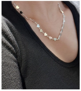 Close-up of S925 silver necklace with heart charms worn on neck over black knitwear