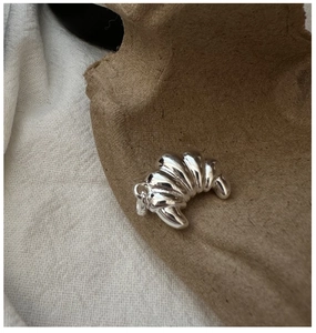 Macro shot of silver croissant pendant with polished mirror finish on rustic tray