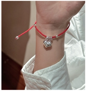 Detail of red braided rope bracelet with polished silver heart pendant on model wrist