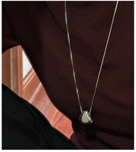 Detail of a minimalist S925 silver water drop pendant worn on a dark red sweater