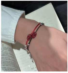 Detail of red and black woven cord bracelets with silver beads and sycee charms on a book