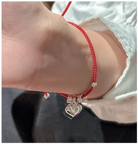 Close-up of a minimalist red braided rope bracelet with a silver heart charm on wrist