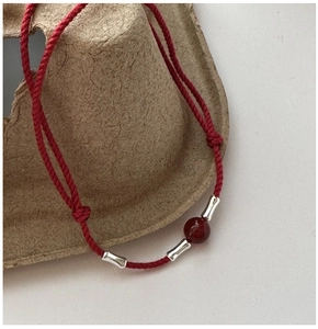 Close-up of red braided rope bracelet with silver bamboo beads and red agate charm