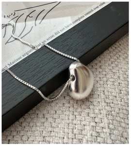 Macro detail of silver minimalist bean pendant on a fine box chain necklace