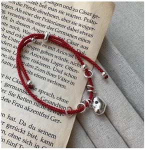 Detail of red woven rope bracelet with silver heart charm on a vintage book page