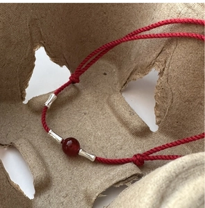 Macro shot of silver bamboo-style beads and red agate on a braided red rope bracelet