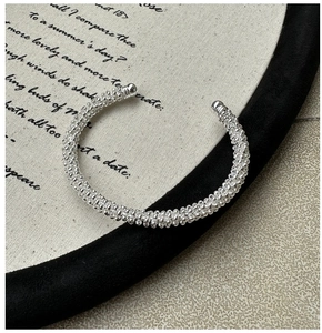 Macro view of C-shaped S925 sterling silver bangle with beaded mesh texture and smooth tips