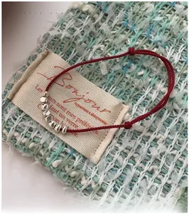 Detail of red braided string bracelet with seven silver beads on tweed fabric background