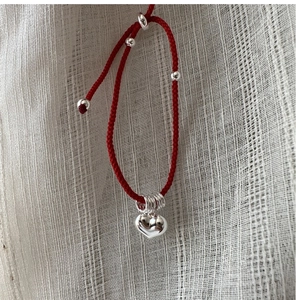 Close-up of red woven cord bracelet with silver heart pendant and polished beads