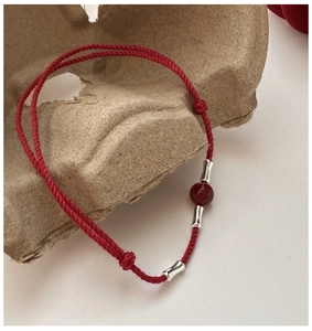 Detail of red braided silk rope bracelet featuring silver bamboo beads and red agate charm
