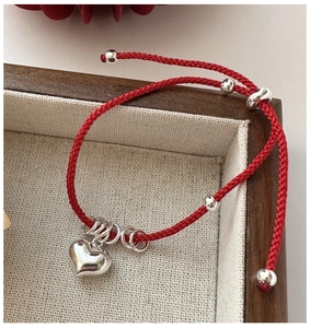 Macro shot of red braided rope bracelet with polished silver heart charm in a wood box