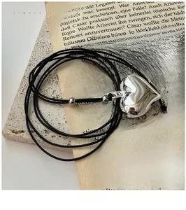 Polished silver heart pendant on a thin black cord resting on vintage textured paper