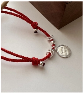 Macro view of silver Good Luck tag on red braided cord bracelet with metal beads