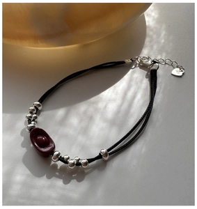 Detail of S925 sterling silver tag and red cinnabar ingot charm on black cord bracelet
