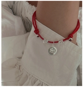 Macro detail of red woven rope bracelet with Good Luck coin pendant and silver beads