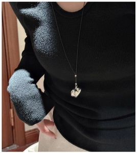 Close-up of polished silver heart pendant on black cord worn by a model in black