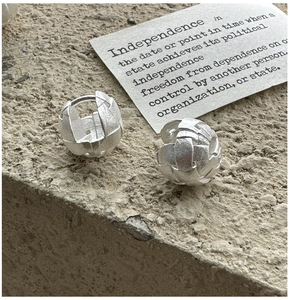 Close-up of S925 sterling silver earrings with woven ball design on stone surface