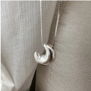 Macro shot of silver crescent moon pendant with brushed metal finish on box chain