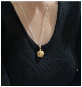 Detailopname van de minimalistische gouden geweven bolhanger aan zilveren ketting