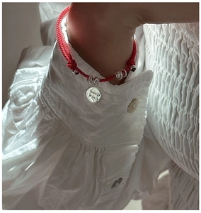 Detailed view of red braided bracelet with silver Good Luck pendant on wrist