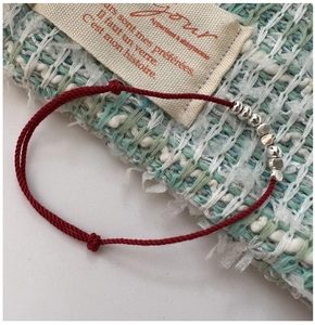 Detailed macro view of red braided rope bracelet with silver beads on textured fabric