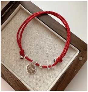 Close-up of red woven silver lucky bracelet with Good Luck engraved pendant