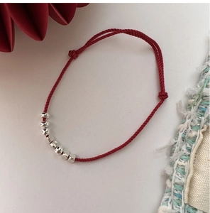 Close-up of minimalist red cord bracelet with 925 sterling silver beads on light background