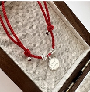 Detail view of red woven bracelet with silver beads and Good Luck engraved tag