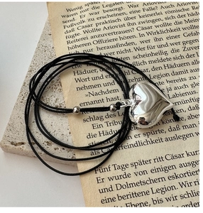Detail view of a polished heart pendant on a black cord over vintage paper background
