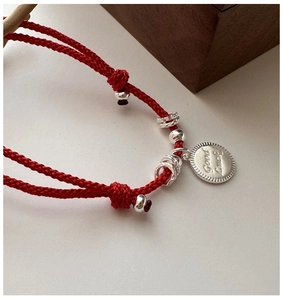 Detail of red braided lucky bracelet with silver Good Luck pendant and bead accents
