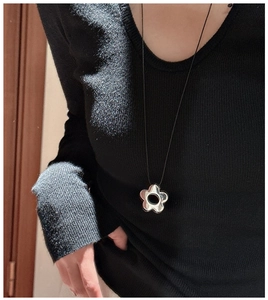 Détail du pendentif fleur argentée ajourée sur cordon noir porté sur un pull