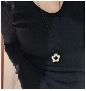 Détail d'un pendentif fleur argenté ajouré sur collier à lacets noirs porté par un mannequin