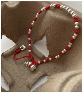 Détail d'un bracelet en corde rouge tressée avec perles d'argent et pendentif gourde