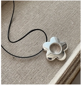 Détail d'un pendentif fleur en argent 925 avec cordon noir sur lin beige