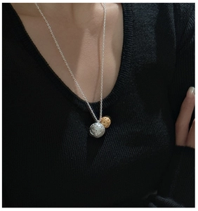 Gros plan de pendentifs foot argent S925 et boule dorée sur un pull en maille noir