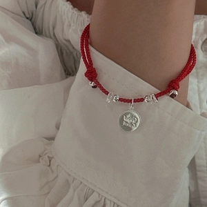 Red cord bracelet with S925 silver Good Luck coin charm on a model's wrist