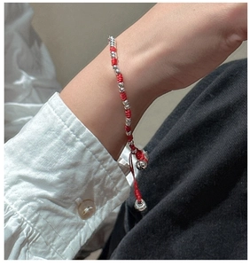 Gros plan d'un bracelet tissé rouge avec perles argentées au poignet sur une manche