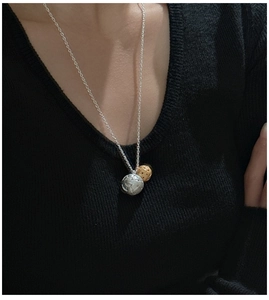 Détail du collier à deux pendentifs sphériques bicolores sur un pull en maille