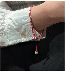 Détail du bracelet en cordon rouge tressé avec perles argentées et breloque réglable